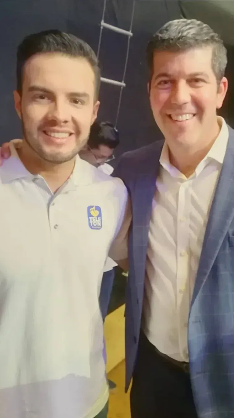 Dos personas, a la izquierda una persona de camisa blanca con el logo de la Teletón salvadoreña y a la derecha Fernando Palomo