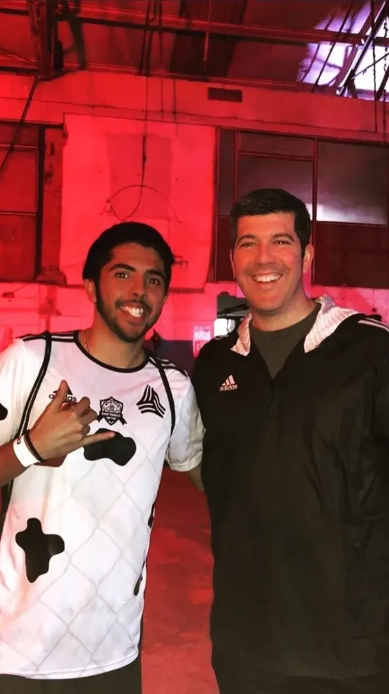 Dos personas en un lugar con luz roja, a la izquierda el usuario miltonl3mus con una camiseta blanca, a la derecha Fernando Palomo