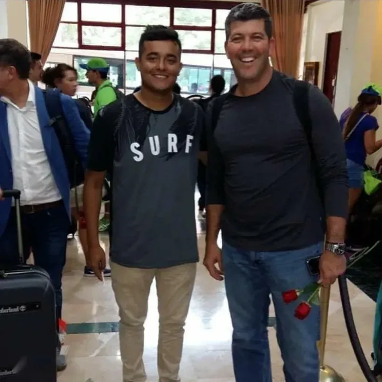 Un evento con muchas personas, usuario binkz12 con una camiseta que dice "SURF" a la izquierda y Fernando Palomo a la derecha con un par de rosas en las manos
