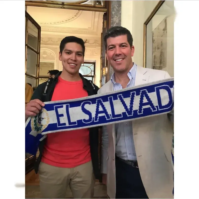 Dos personas sosteniendo un banda de El Salvador, a la derecha Fernando Palomo